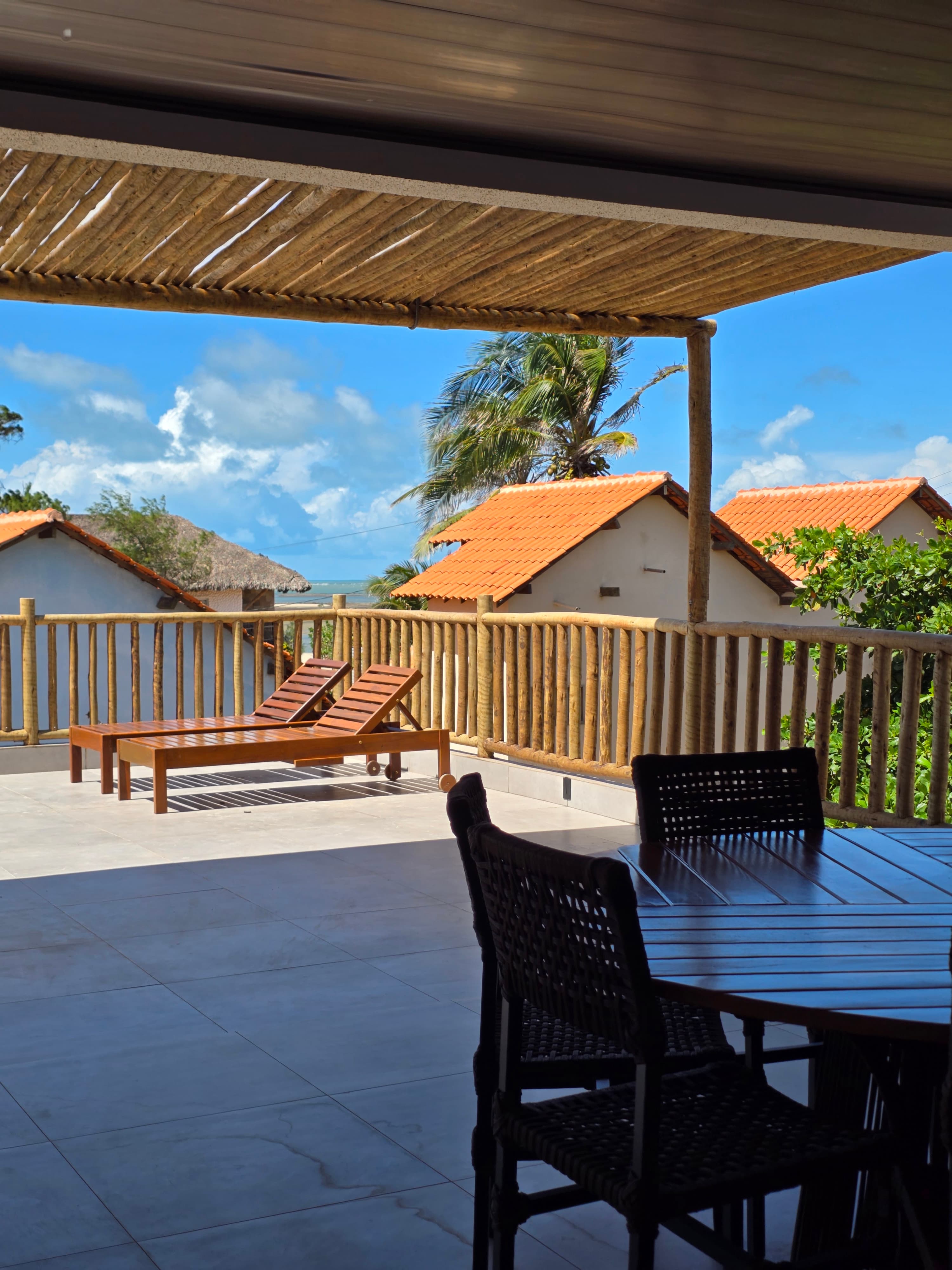 Sunny patio with wooden lounge chairs and dining set overlooking tropical villas and palm trees.