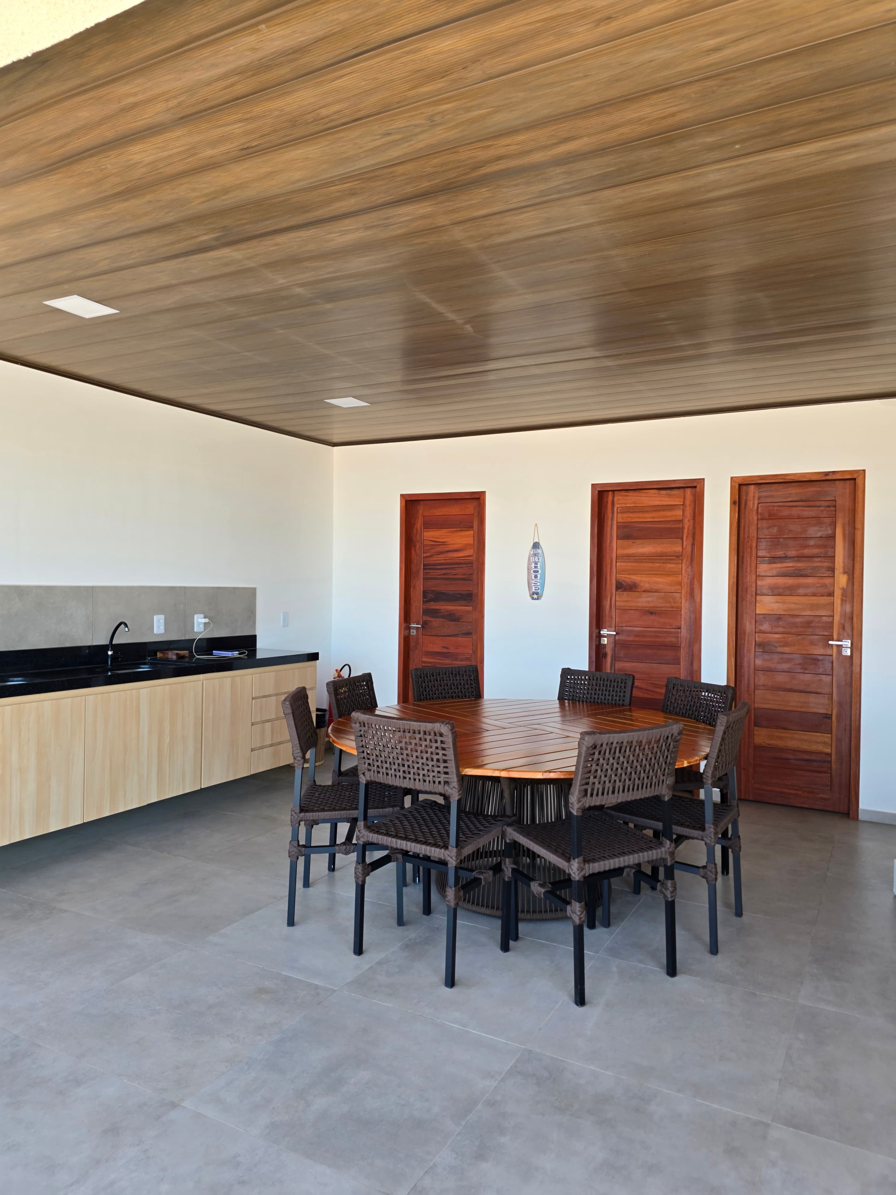 Modern dining area with a wooden table, woven chairs, wood-paneled ceiling, and three wooden doors.