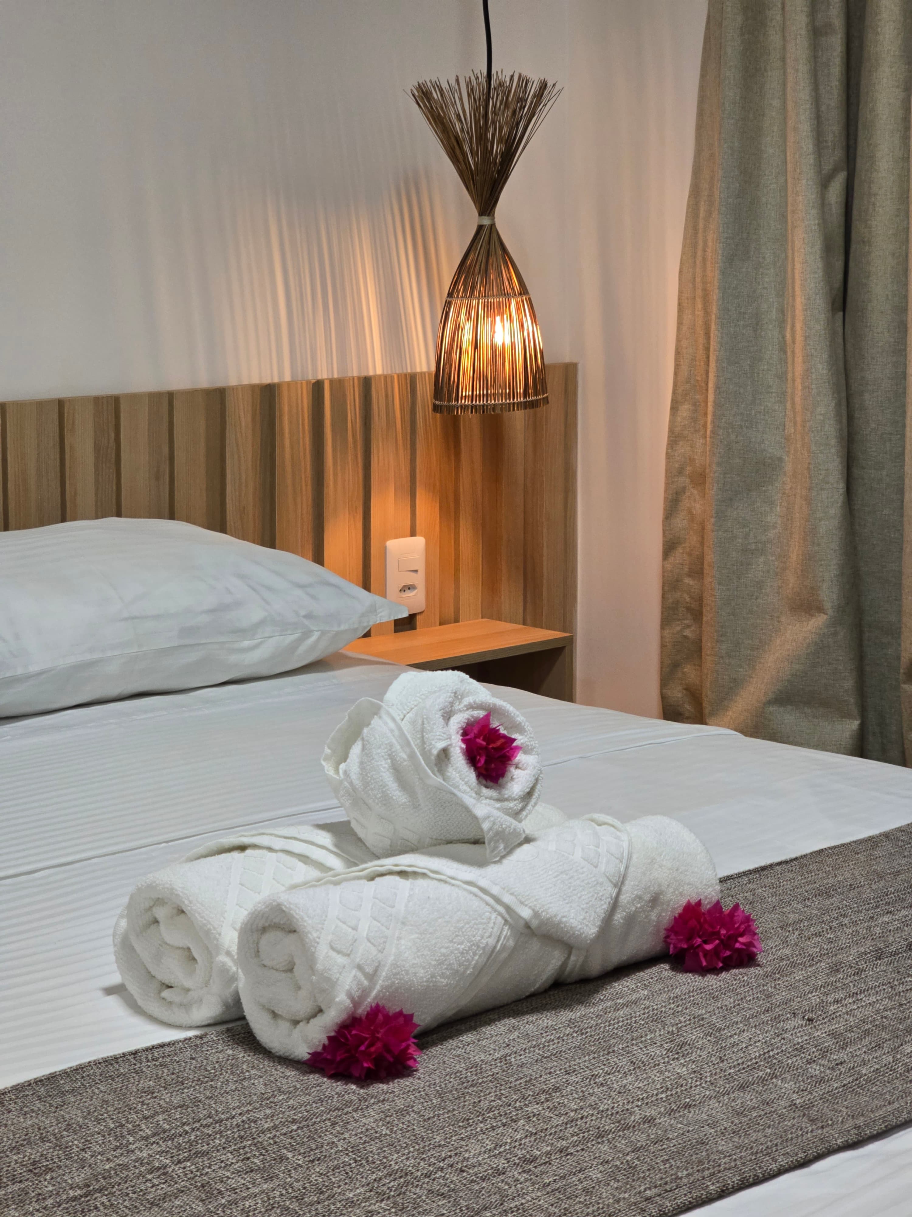Rolled white towels with pink flowers on a bed beside a warm, glowing wicker lamp.
