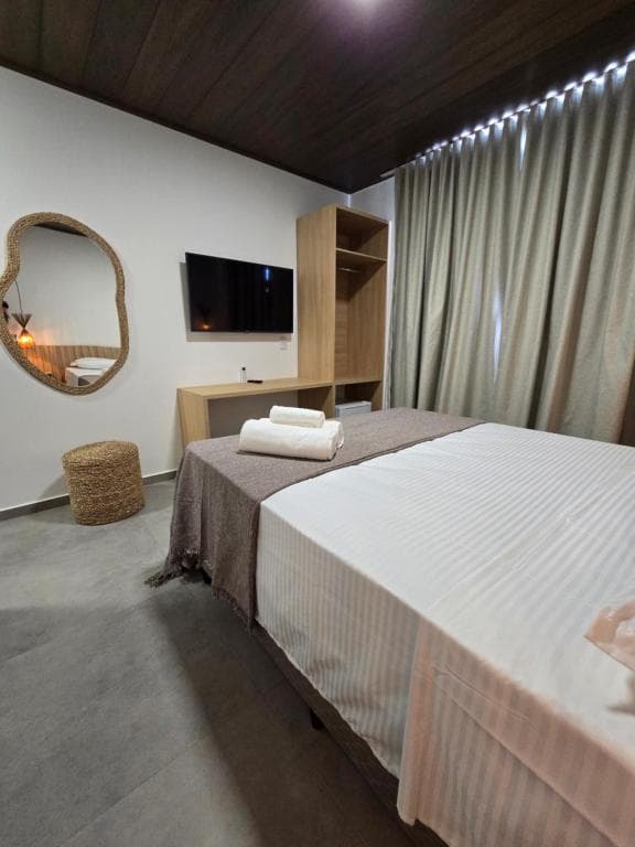 Minimalist hotel room featuring white striped linens, wooden furniture, and a large woven mirror.
